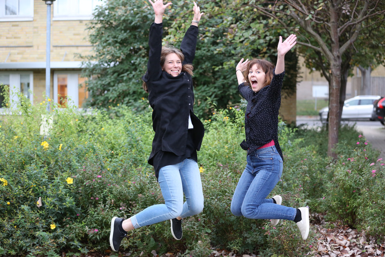 Två kvinnor i blå jeans och svarta skjortor hoppar högt upp i luften.