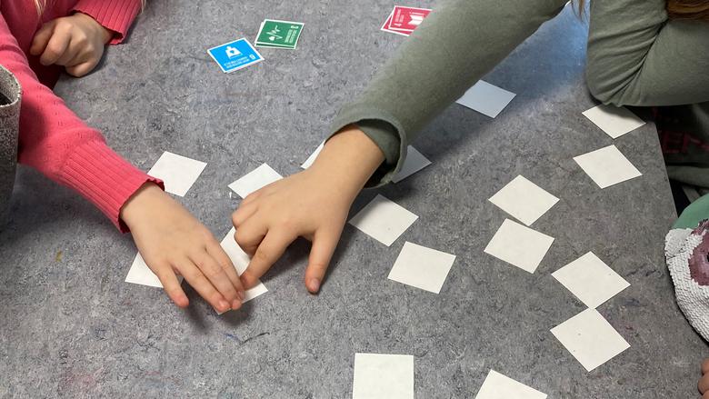 Två barnhänder vänder vita fyrkantiga lappar som ligger på golvet. Bilden visar spelet Memory. 