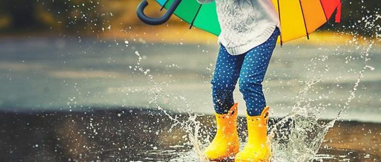 Barn som plaskar i vattenpöl med gummistövlar och paraply.