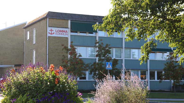 Fasaden på kommunhuset i Lomma i gult tegel och tre våningar, Lomma kommuns logotyp i form av ett rött ankare högst upp till vänster på byggnaden.