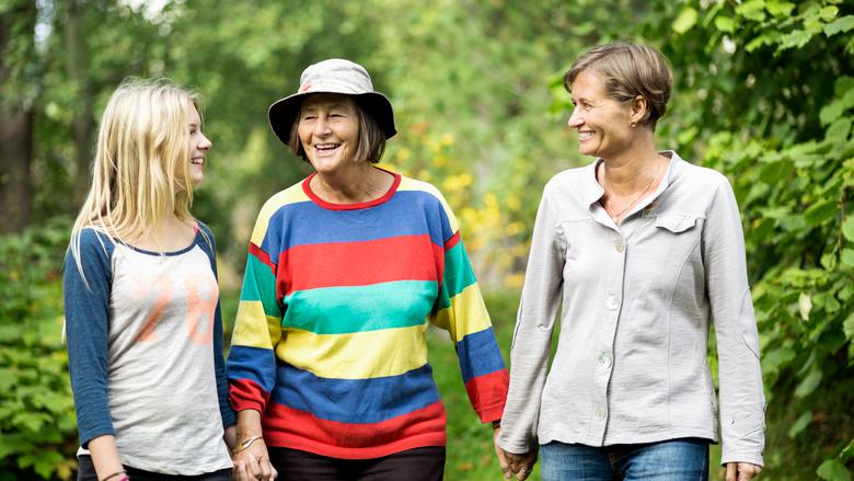 Tre generationer kvinnor som går i en park med gröna växter