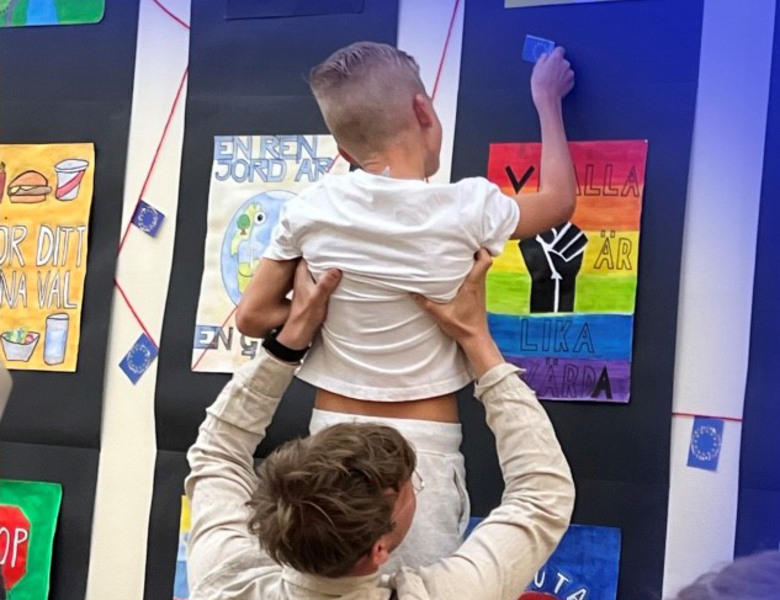 Elev lyfts upp av pedagog och sätter en EU-flagga på väggen.
