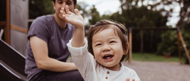 Barn som skrattar mot kameran med förälder på lekplats