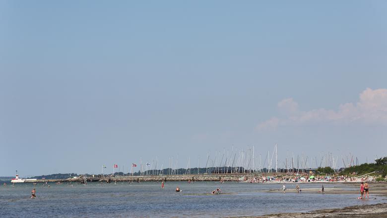 Strand med badgäster i bakgrunden syns segelbåtar