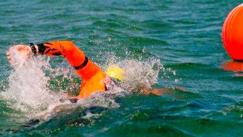 Person simmar i öppet vatten i orange simdräkt mot en orange boj.