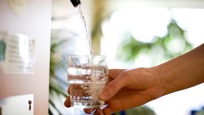 En hand håller ett glas vatten under en rinnande vattenstråle.