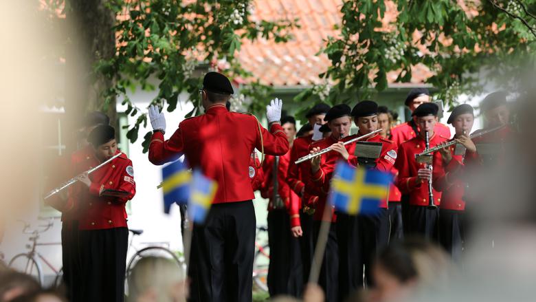 Orkester med ungdomar klädda i röda skjortor och svarta byxor spelar blåsinstrument.