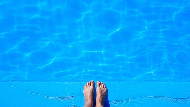 Fötter i vatten i en blå pool