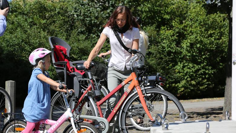 En vuxen och ett barn som parkerar sina cyklar i ett cykelställ. 