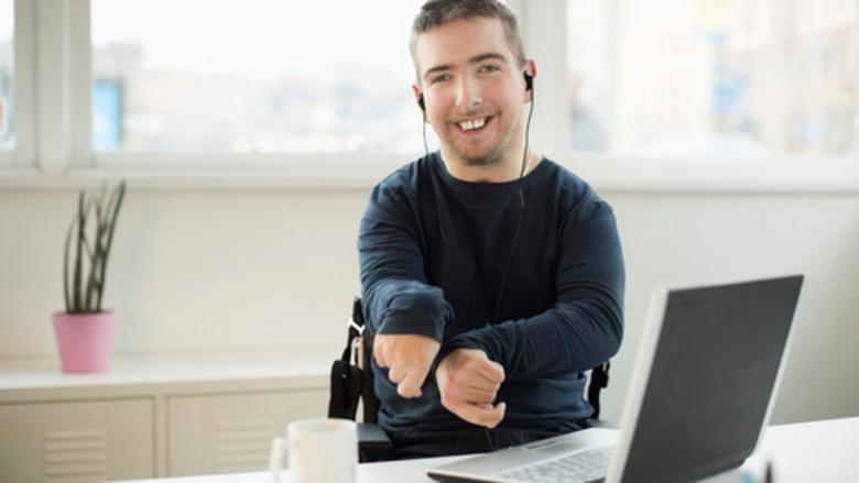 Kiolle med händerna knutna utåt sitter framför en laptop. Bilden illustrerar person med funktionshinder..
