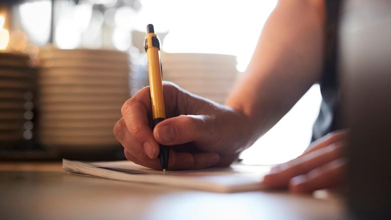 Närbild på en hand som skriver med gul penna på ett papper.