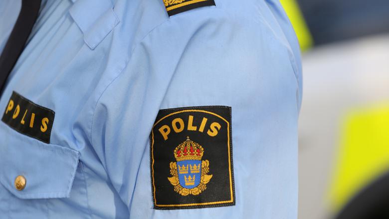 Närbild på ett mörkt polismärke som sitter på en polismans ljusblå skjorta. Polis är skrivet i versaler. Bilden symboliserar Polisen som yrkesgrupp.