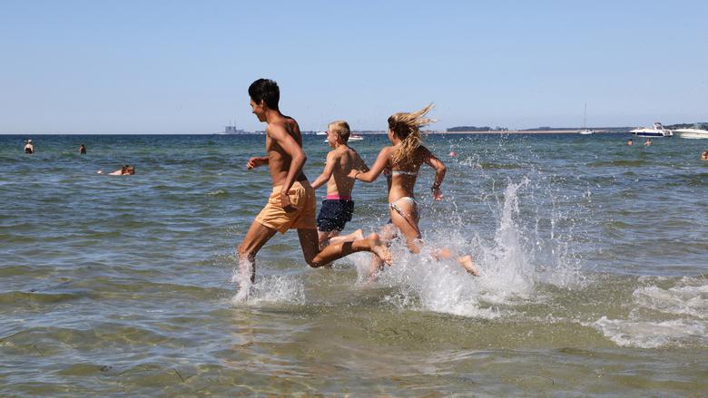 Ungdomar som springer i vattnet på stranden.