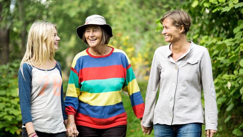 Tre kvinnor i olika åldrar hand i hand gående utomhus.