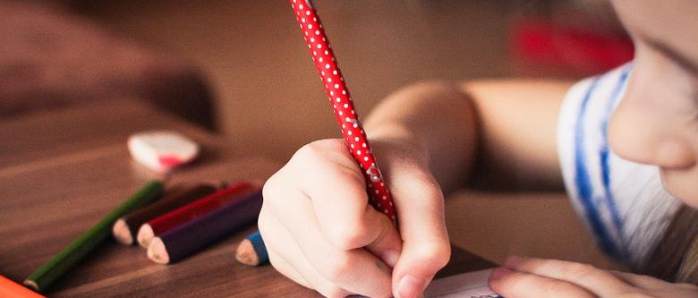 Ett barn sitter vid skrivbordet och skriver med färgglada pennor