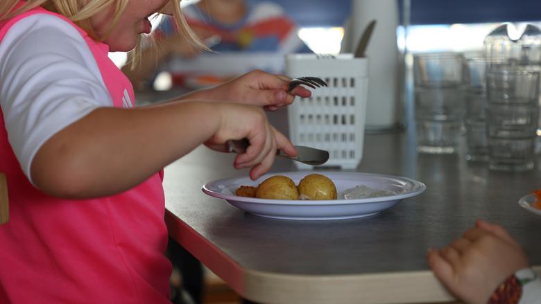 Barnhänder skär kokt potatis med kniv och gaffel.